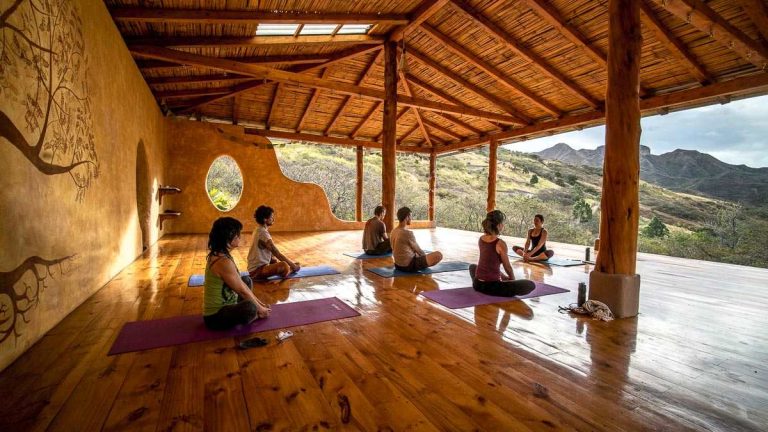 a group of people sitting on yoga mats in an open air pavilion at eco-resort Izhcayluma